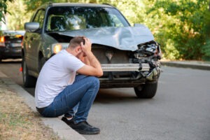 A man by his car after a head-on collision. In this situation, you can contact a head-on collision lawyer.