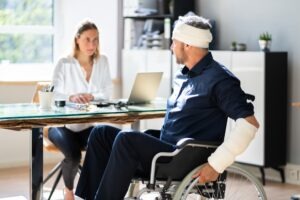 A man in a wheelchair with a bandaged head is meeting with a female attorney.