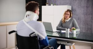 A lawyer sitting with an injured client wearing a neck brace and a sling, and explaining what they can sue for after a car accident.